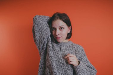 Genç kız sıcak gri süveterli kadın örme kazaklı kısa saç kesimi, metin için yer ile turuncu arka plan üzerinde poz