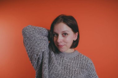 Genç kız sıcak gri süveterli kadın örme kazaklı kısa saç kesimi, metin için yer ile turuncu arka plan üzerinde poz