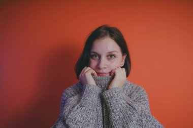 Genç kız sıcak gri süveterli kadın örme kazaklı kısa saç kesimi, metin için yer ile turuncu arka plan üzerinde poz