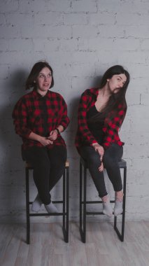 Kırmızı ve siyah ekose gömlekler tuğla duvar arka plan, arkadaşlık kavramı üzerinde sandalyelere oturan iki genç kız