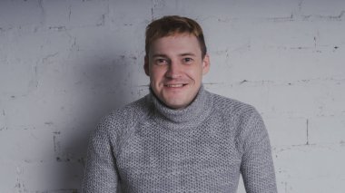 Sandalyeye gri bir arka plan üzerinde sıcak kazaklı adam. Bir adam bir tuğla duvara poz.