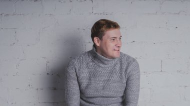 Sandalyeye gri bir arka plan üzerinde sıcak kazaklı adam. Bir adam bir tuğla duvara poz.