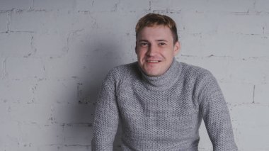 Sandalyeye gri bir arka plan üzerinde sıcak kazaklı adam. Bir adam bir tuğla duvara poz.