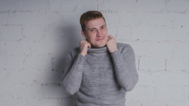 Sandalyeye gri bir arka plan üzerinde sıcak kazaklı adam. Bir adam bir tuğla duvara poz.