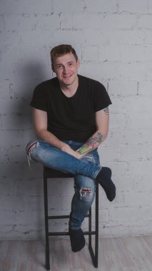 Siyah bir tişört, bir gri tuğla duvara yakışıklı bir adam. Acımasız adam dövme olan