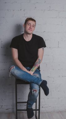 Siyah bir tişört, bir gri tuğla duvara yakışıklı bir adam. Acımasız adam dövme olan