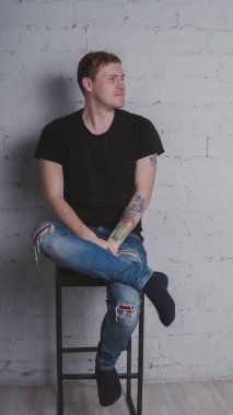 Siyah bir tişört, bir gri tuğla duvara yakışıklı bir adam. Acımasız adam dövme olan