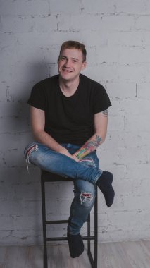 Siyah bir tişört, bir gri tuğla duvara yakışıklı bir adam. Acımasız adam dövme olan