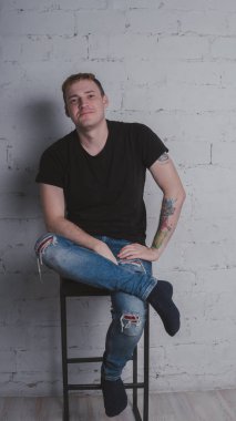 Siyah bir tişört, bir gri tuğla duvara yakışıklı bir adam. Acımasız adam dövme olan