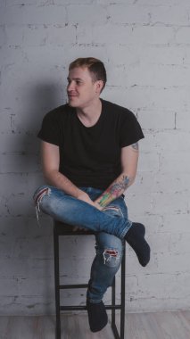 Siyah bir tişört, bir gri tuğla duvara yakışıklı bir adam. Acımasız adam dövme olan