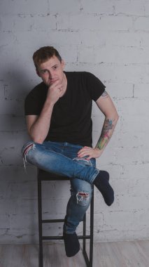 Siyah bir tişört, bir gri tuğla duvara yakışıklı bir adam. Acımasız adam dövme olan