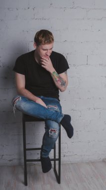 Siyah bir tişört, bir gri tuğla duvara yakışıklı bir adam. Acımasız adam dövme olan