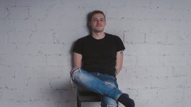 Siyah bir tişört, bir gri tuğla duvara yakışıklı bir adam. Acımasız adam dövme olan