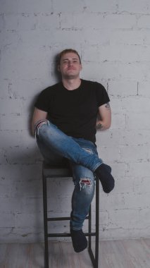 Siyah bir tişört, bir gri tuğla duvara yakışıklı bir adam. Acımasız adam dövme olan