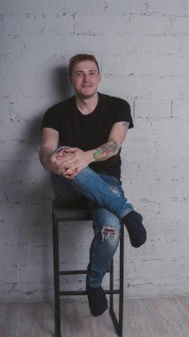 Siyah bir tişört, bir gri tuğla duvara yakışıklı bir adam. Acımasız adam dövme olan