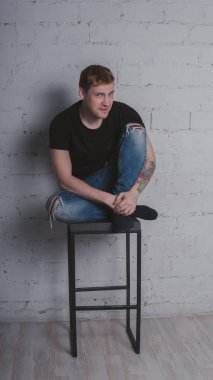 Siyah bir tişört, bir gri tuğla duvara yakışıklı bir adam. Acımasız adam dövme olan