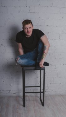 Siyah bir tişört, bir gri tuğla duvara yakışıklı bir adam. Acımasız adam dövme olan