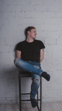 Siyah bir tişört, bir gri tuğla duvara yakışıklı bir adam. Acımasız adam dövme olan