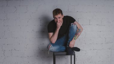 Siyah bir tişört, bir gri tuğla duvara yakışıklı bir adam. Acımasız adam dövme olan