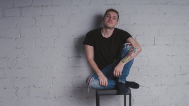 Siyah bir tişört, bir gri tuğla duvara yakışıklı bir adam. Acımasız adam dövme olan