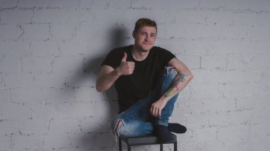 Siyah bir tişört, bir gri tuğla duvara yakışıklı bir adam. Acımasız adam dövme olan