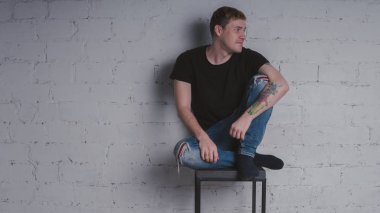 Siyah bir tişört, bir gri tuğla duvara yakışıklı bir adam. Acımasız adam dövme olan