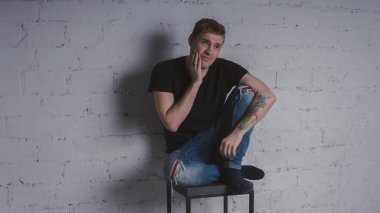 Siyah bir tişört, bir gri tuğla duvara yakışıklı bir adam. Acımasız adam dövme olan