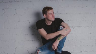 Siyah bir tişört, bir gri tuğla duvara yakışıklı bir adam. Acımasız adam dövme olan