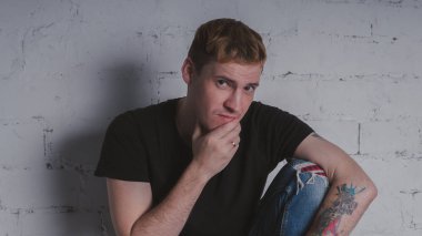 Siyah bir tişört, bir gri tuğla duvara yakışıklı bir adam. Acımasız adam dövme olan