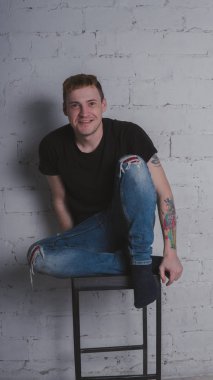 Siyah bir tişört, bir gri tuğla duvara yakışıklı bir adam. Acımasız adam dövme olan