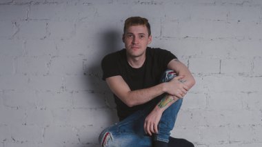 Siyah bir tişört, bir gri tuğla duvara yakışıklı bir adam. Acımasız adam dövme olan