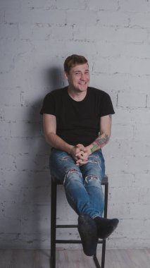 Siyah bir tişört, bir gri tuğla duvara yakışıklı bir adam. Acımasız adam dövme olan