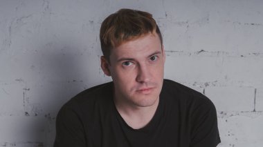 Siyah bir tişört, bir gri tuğla duvara yakışıklı bir adam. Acımasız adam dövme olan