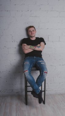 Siyah bir tişört, bir gri tuğla duvara yakışıklı bir adam. Acımasız adam dövme olan