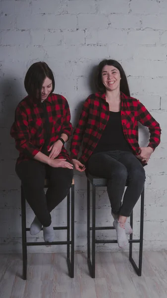 レンガ壁の背景 女性の友情の概念に椅子に座って赤と黒の格子縞のシャツの つの若い女の子 — ストック写真