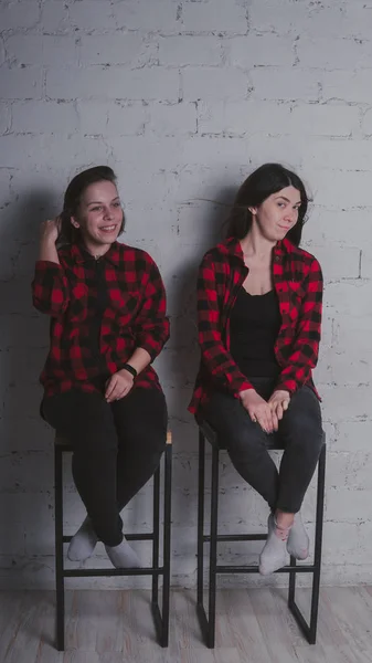 レンガ壁の背景 女性の友情の概念に椅子に座って赤と黒の格子縞のシャツの つの若い女の子 — ストック写真
