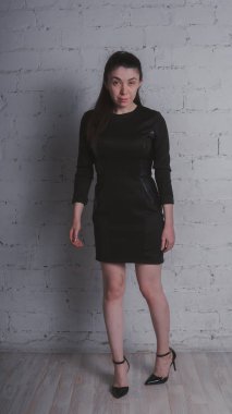 Kız beyaz duvara karşı poz. Siyah elbise modeli. Esmer Doğu görünüyor.