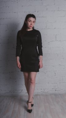 Kız beyaz duvara karşı poz. Siyah elbise modeli. Esmer Doğu görünüyor.