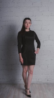 Kız beyaz duvara karşı poz. Siyah elbise modeli. Esmer Doğu görünüyor.