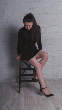 Kız beyaz duvara karşı poz. Siyah elbise modeli. Esmer Doğu görünüyor.