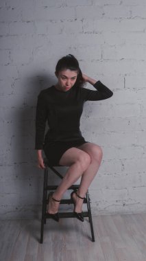 Kız beyaz duvara karşı poz. Siyah elbise modeli. Esmer Doğu görünüyor.