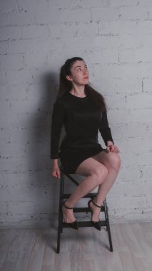 Kız beyaz duvara karşı poz. Siyah elbise modeli. Esmer Doğu görünüyor.