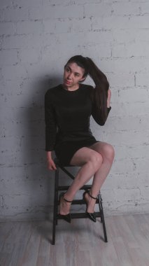 Kız beyaz duvara karşı poz. Siyah elbise modeli. Esmer Doğu görünüyor.