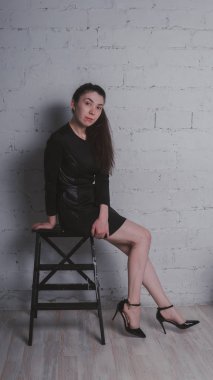 Kız beyaz duvara karşı poz. Siyah elbise modeli. Esmer Doğu görünüyor.