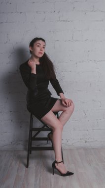 Kız beyaz duvara karşı poz. Siyah elbise modeli. Esmer Doğu görünüyor.