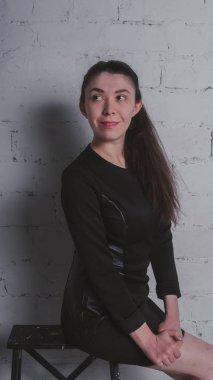 Kız beyaz duvara karşı poz. Siyah elbise modeli. Esmer Doğu görünüyor.