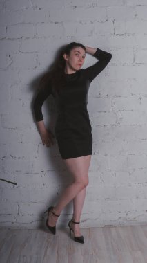 Kız beyaz duvara karşı poz. Siyah elbise modeli. Esmer Doğu görünüyor.