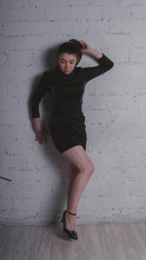 Kız beyaz duvara karşı poz. Siyah elbise modeli. Esmer Doğu görünüyor.