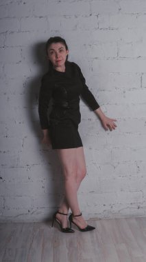 Kız beyaz duvara karşı poz. Siyah elbise modeli. Esmer Doğu görünüyor.