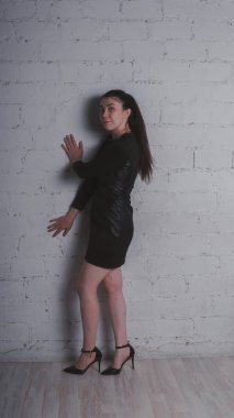 Kız beyaz duvara karşı poz. Siyah elbise modeli. Esmer Doğu görünüyor.